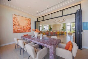 Uma sala de jantar espaçosa com uma mesa e cadeiras de mármore, um quadro abstrato grande na parede e vista para uma sala de estar luminosa.