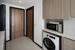 A compact kitchen with a washing machine, microwave, and cabinets.