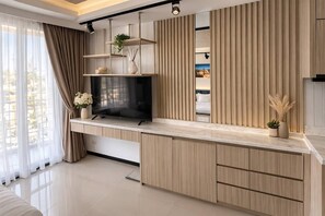 A modern living room with a flat-screen TV, wooden cabinets, and a large window with curtains.