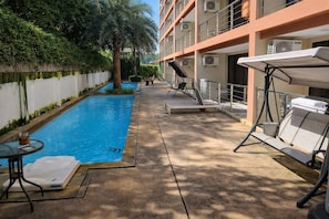 A pool area with lounge chairs and a table, surrounded by a building with balconies and air conditioning units. - Studio Coral 1br | Mountain view | rbc rawai beach (Rawai)