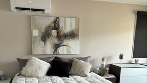 Un dormitorio con una cama grande, un cuadro en la pared, un escritorio con lámpara y una ventana.