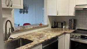 Una cocina moderna con armarios blancos, encimeras de granito y electrodomésticos de acero inoxidable, además de un reloj visible.