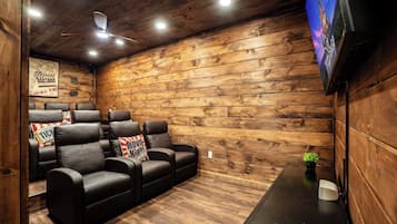 Ein Zimmer mit Holzvertäfelung, einem Deckenventilator, einem Flachbildfernseher und einer Sitzecke mit Ledersesseln und einem kleinen Tisch.