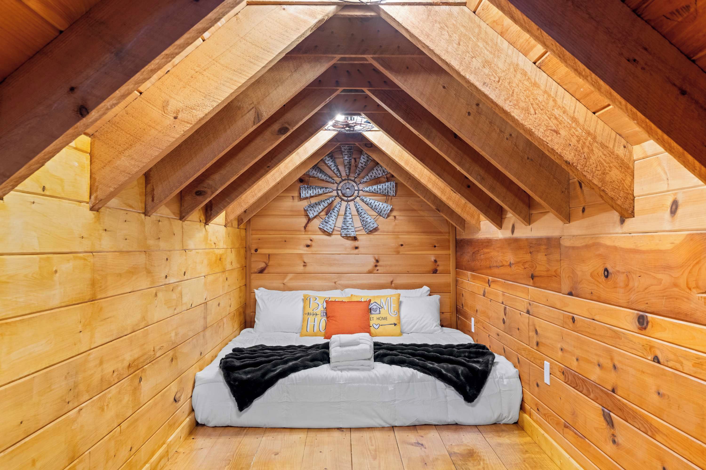Ein gemütliches Schlafzimmer im Dachgeschoss mit schrägen Wänden, Holzwänden, einem Bett mit weißer Bettwäsche und einer dekorativen Holzdekorleiste an der Decke.