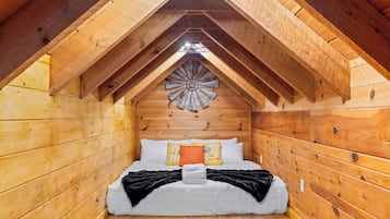 Ein gemütliches Schlafzimmer im Dachgeschoss mit schrägen Wänden, Holzwänden, einem Bett mit weißer Bettwäsche und einer dekorativen Holzdekorleiste an der Decke.