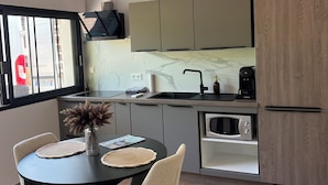 Una cocina moderna con horno empotrado, microondas y lavamanos. Hay una zona de comedor con una mesa redonda y sillas, y un florero con flores secas.