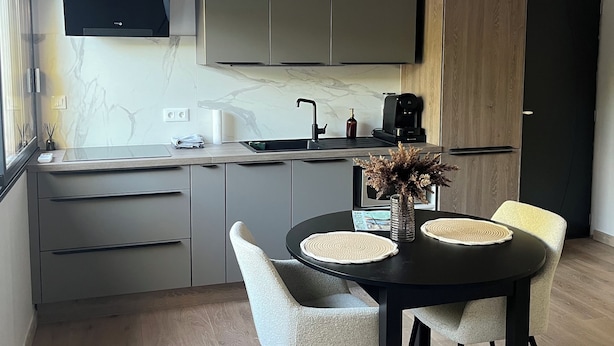 Una cocina moderna con armarios grises, una campana extractora negra y una zona de comedor con una mesa redonda y cuatro sillas.