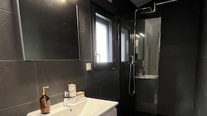 Un baño moderno con un tocador blanco, una cabina de ducha con mampara de cristal y un espejo grande sobre el lavamanos.
