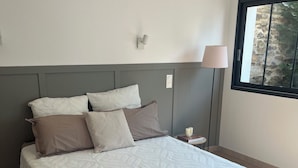 Un dormitorio con una cama grande, una mesita de noche, una lámpara y una ventana con vistas al verdor.