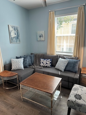 Ein Wohnzimmer mit einer Eckcouch, zwei Couchtischen und Kunstwerken an den Wänden.