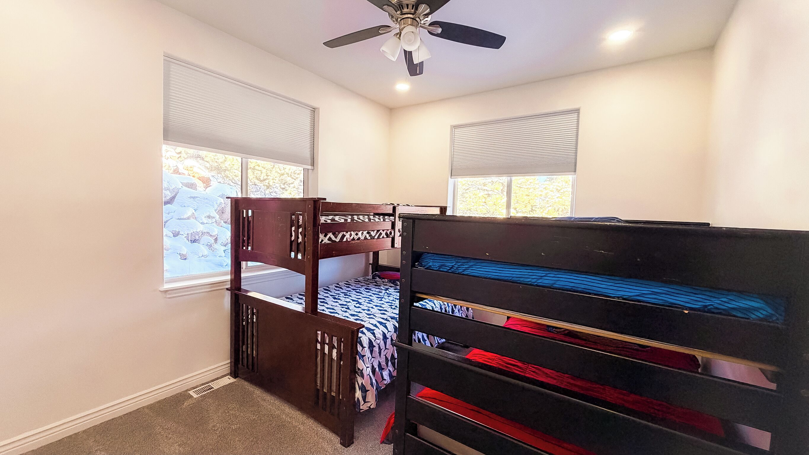 A bedroom with two bunk beds, a ceiling fan, and windows with blinds.