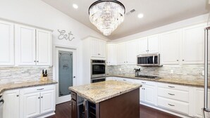 A modern kitchen with white cabinetry, granite countertops, a central island, stainless steel appliances, and a chandelier. - 7BR Ski & Golf Course Retreat with Hot Tub (Flagstaff)
