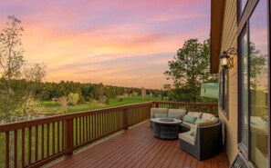 A deck with outdoor seating, a view of a park, and a building with a large window. - 7BR Ski & Golf Course Retreat with Hot Tub (Flagstaff)