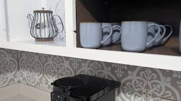 Une cuisine équipée d’une machine à café Keurig, d’une bouilloire et d’une étagère où sont rangées des serviettes pliées et des tasses.