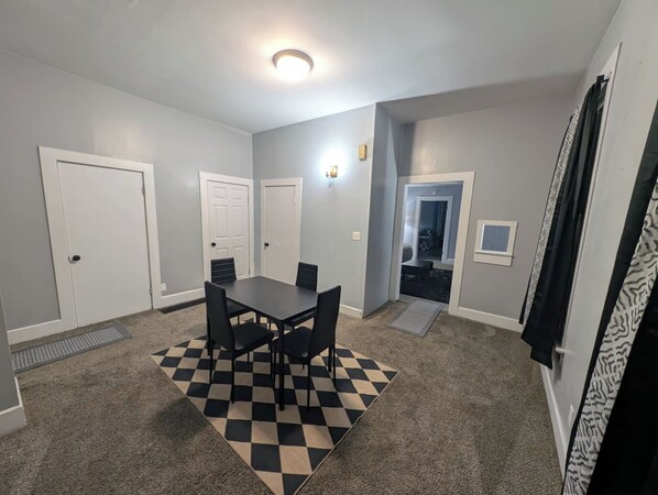 A room with a checkered rug, a table with chairs, and a door leading to another room.