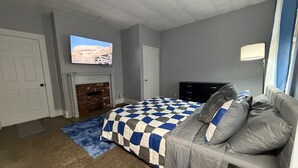 Ein Schlafzimmer mit einem Bett, einem Sofa, einem Fernseher über einem Kamin und einer Tür.