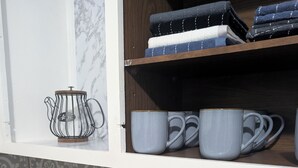 Eine Küche mit Kaffeemaschine, Wasserkocher und einem Regal mit gefalteten Handtüchern.
