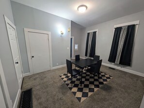 A room with a checkered carpet, a dining table with chairs, a white door, and a window with curtains. - Work Crews: Clean 2BR near US-41 + Laundry & TVs (Evansville)