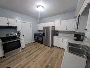 A compact kitchen with white cabinets, a stainless steel refrigerator, an oven, a washing machine, and a sink.