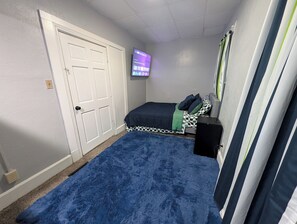 Ein Schlafzimmer mit einem Bett, einem an der Wand befestigten Fernseher, einem blauen Teppich und einer Tür.