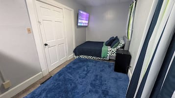 Une chambre à coucher avec un lit, un téléviseur fixé au mur, une porte et une fenêtre avec des rideaux.