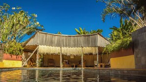 A thatched-roof structure with a pool in front. - résidence Ambalamanga (Nosy Be)