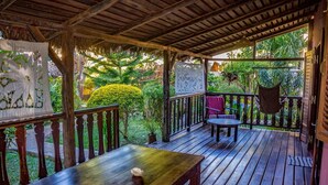 A wooden deck with a table and chairs, surrounded by lush greenery and a thatched roof structure. - résidence Ambalamanga (Nosy Be)