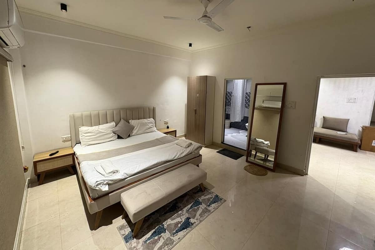 A modern bedroom with a large bed, a ceiling fan, a mirror, and a seating area.