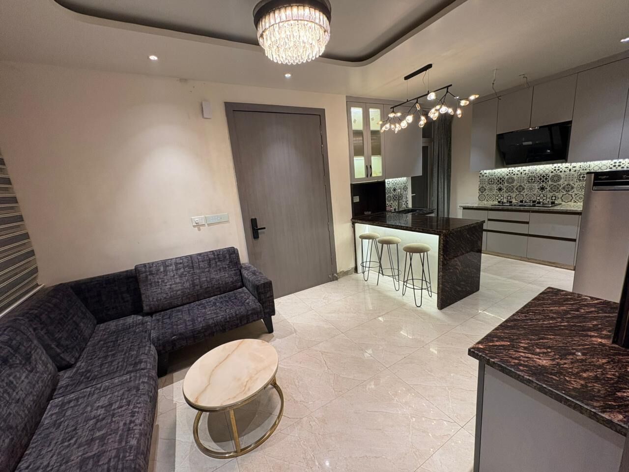 Een moderne woonkamer met een hoekbank, een ronde salontafel en een keuken met barstoelen.