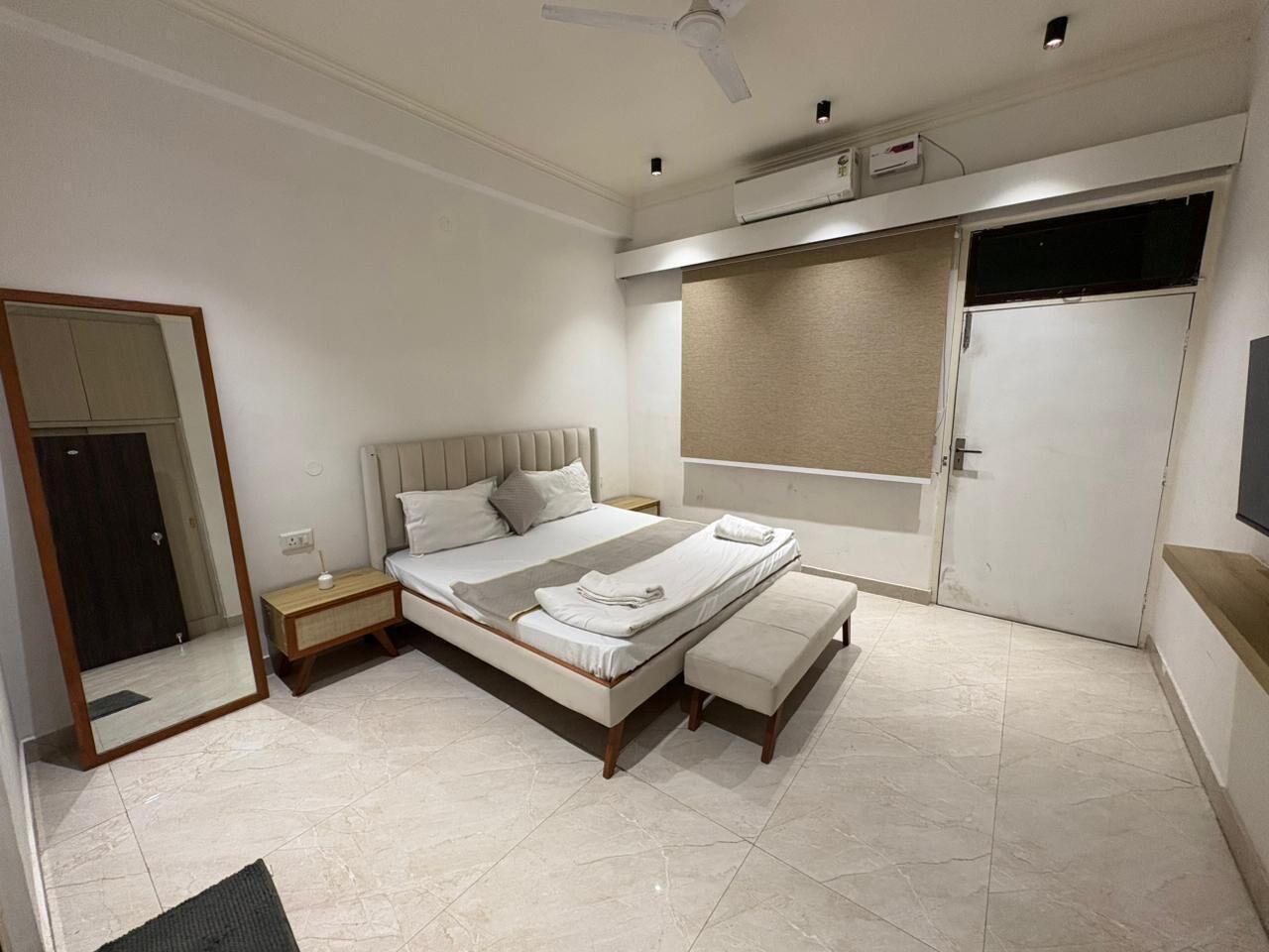 A modern bedroom with a bed, bedside tables, a bench, a mirror, and a wardrobe.