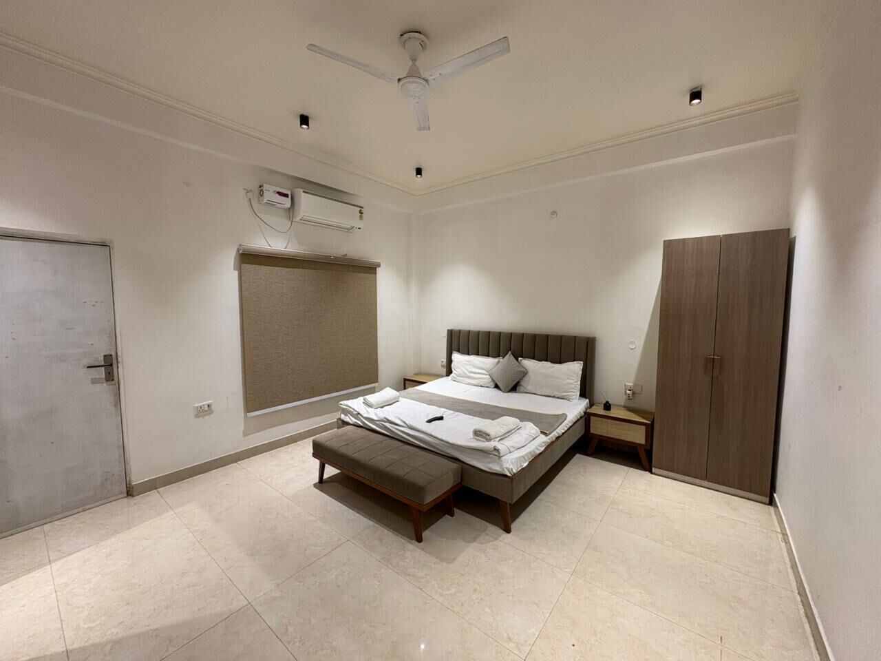 Un dormitorio con cama, banca, armario, espejo de armario, mesita de noche y ventilador de techo.