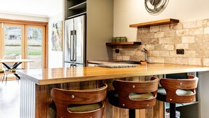 A modern kitchen with a large island, wooden bar stools, a stone backsplash, and a stainless steel refrigerator. - Buffalo Bliss - Magical views (Porepunkah)