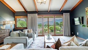 A spacious living room with a large sliding glass door leading to a balcony, a flat-screen TV mounted on the wall, and a chandelier. - Buffalo Bliss - Magical views (Porepunkah)