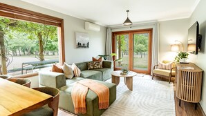 A modern living room with a sofa, coffee table, and a dining area. There are large windows providing a view of the outdoors. - Buffalo Bliss - Magical views (Porepunkah)