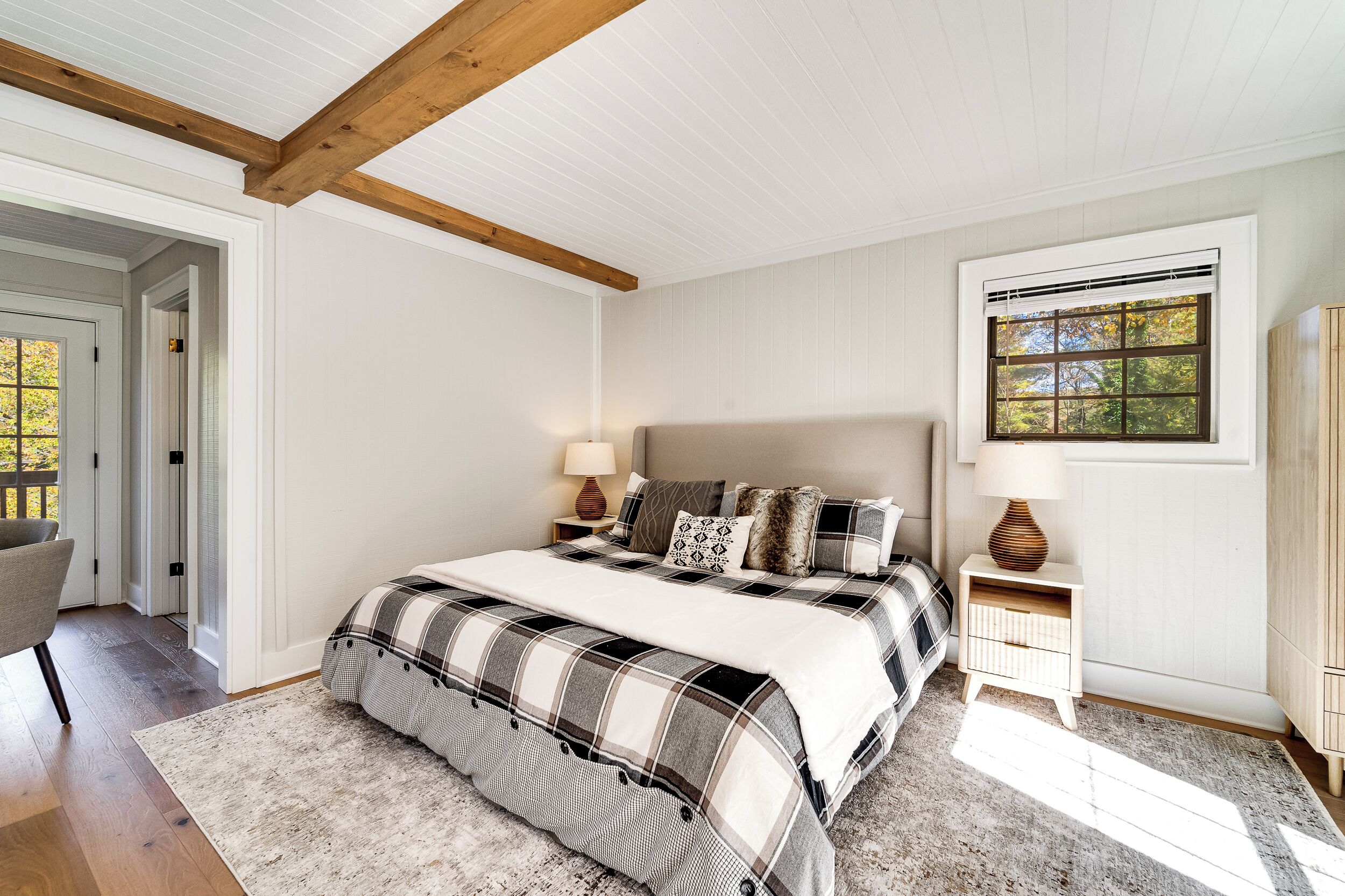 Une chambre à coucher avec un grand lit, une table de chevet, une lampe et une fenêtre donnant sur des arbres.