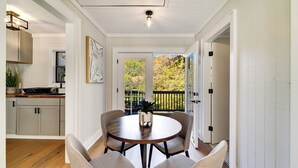 A dining area with a round table and four chairs, a kitchen with cabinets and a countertop, and a view of a balcony with a railing. - Cozy Mountain Cottage Near Downtown (Highlands)