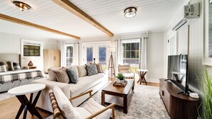 A spacious living room with a sofa, coffee table, and armchair, wooden beams on the ceiling, and large windows. - Cozy Mountain Cottage Near Downtown (Highlands)