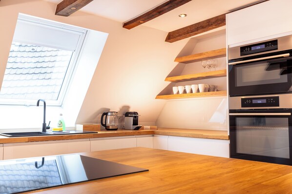 A modern kitchen with a wooden countertop, built-in oven, and a coffee maker. - Fachwerk Boutique Hotel by corents (Hattingen)