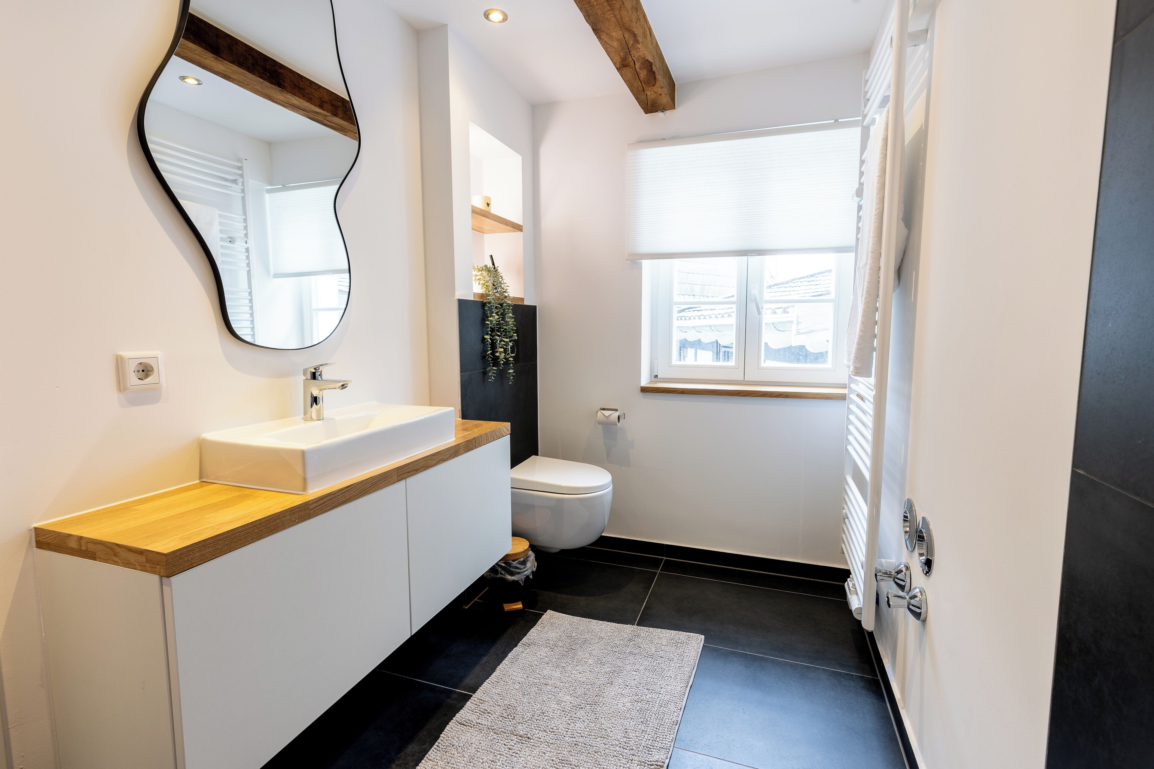 Une salle de bain moderne avec un plan de toilette en bois, un lavabo blanc, des toilettes et un grand miroir.