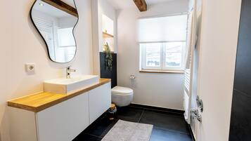 Ein modernes Badezimmer mit Holztischplatte, Waschbecken in Weiß, Toilette und großem Spiegel.