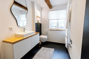 A modern bathroom with a wooden countertop, a white sink, a toilet, and a large mirror. - Fachwerk Boutique Hotel by corents (Hattingen)