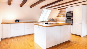 A modern kitchen with wooden beams, white cabinetry, a central island, and built-in appliances. - Fachwerk Boutique Hotel by corents (Hattingen)