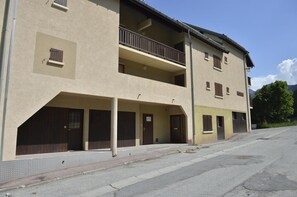 Ein zweistöckiges Gebäude mit Balkon im zweiten Stock, überdachter Eingang und Parkplatz davor.