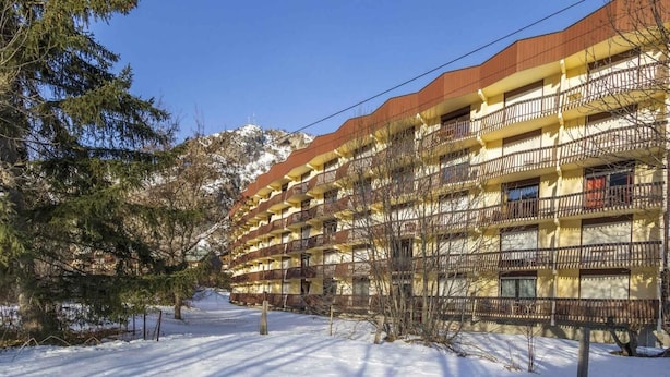 A multi-story hotel with balconies, a snow-covered ground, and a mountain in the background. - 350m from ski slopes, 1st floor, balcony, parking, tv, ski locker, 55m², Valloire (Valloire)
