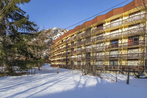 Ein mehrstöckiges Hotel mit Balkonen, verschneitem Untergrund und einem Berg im Hintergrund.