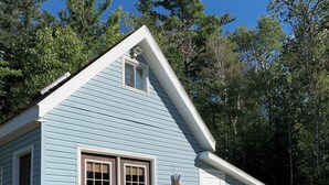 A light blue wooden cabin with a porch and a wooden deck.