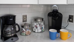 Ett kök med en kaffebryggare, en Keurig-kaffemaskin, en burk med kaffekapslar och två muggar.