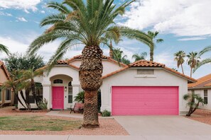 A residential house with a red garage door, a pink door, and a palm tree in the front yard. - Modern Oasis, Heated Pool & Spa (Phoenix)