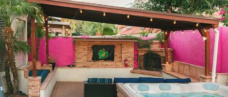 A hot tub area with a stone fireplace, outdoor seating, and a pergola with string lights.
