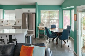 A modern kitchen with white cabinets, a stainless steel refrigerator, and a dining area with a round table and chairs. - Modern Oasis, Heated Pool & Spa (Phoenix)